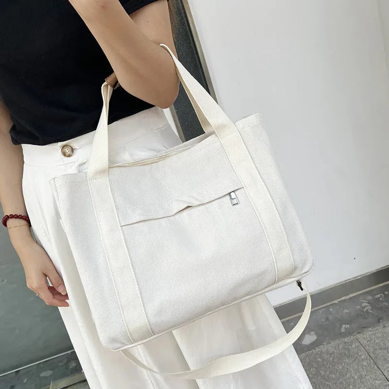 Army green canvas tote bag with open zip sides showing internal laptop and camera pockets.