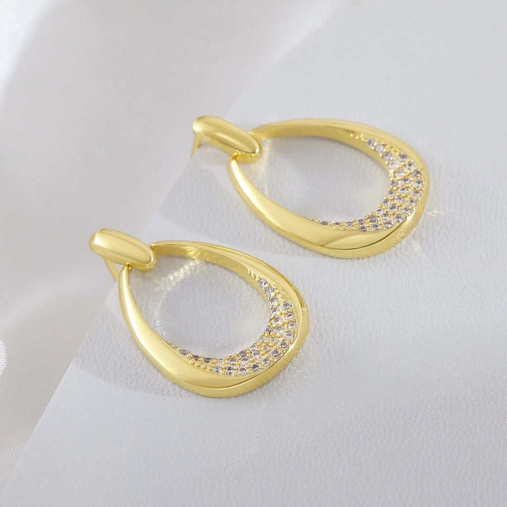 Women's yellow gold geometric drop-shaped earrings with ring design and zircon accents on a white background.