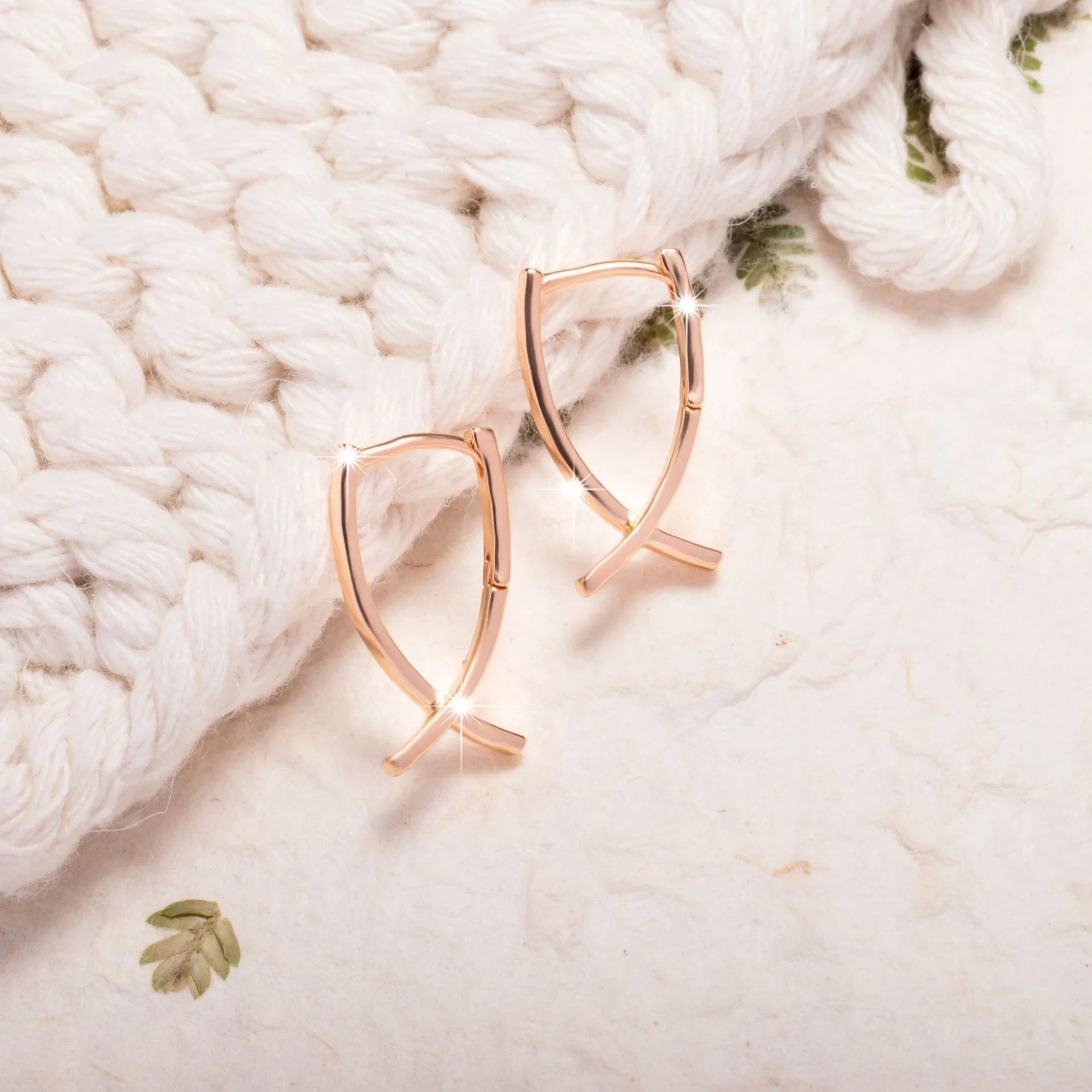 A pair of rose gold cross shaped earrings made from copper on a plain background.