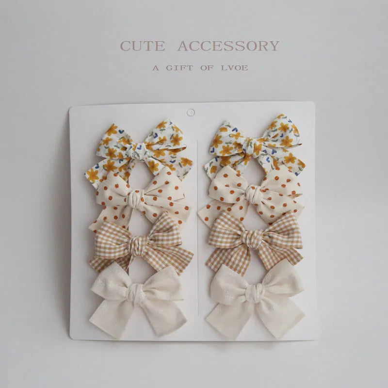 Set of eight children's cloth bow hairclips in assorted colours including beige, blue flowers, and polka dots.