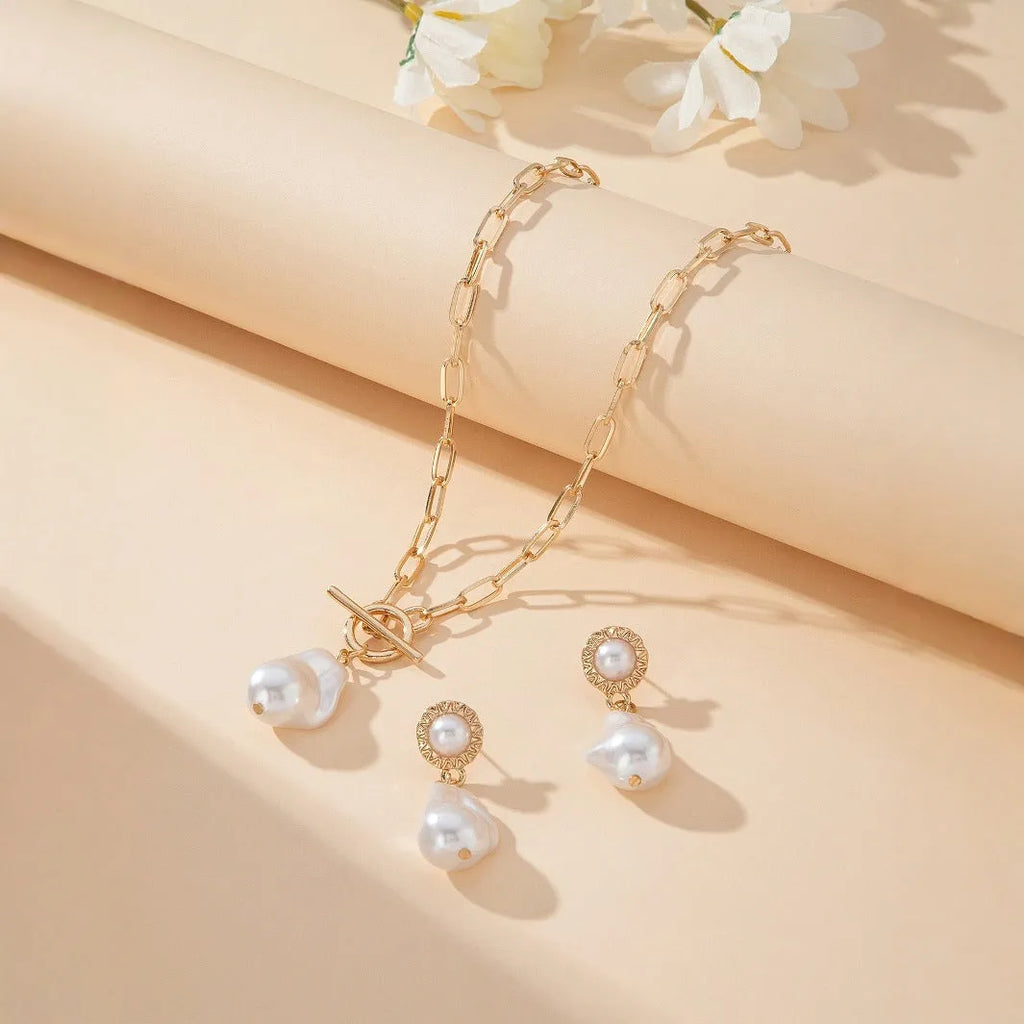 Gold baroque pearl pendant necklace and ear stud set for women on a white background.