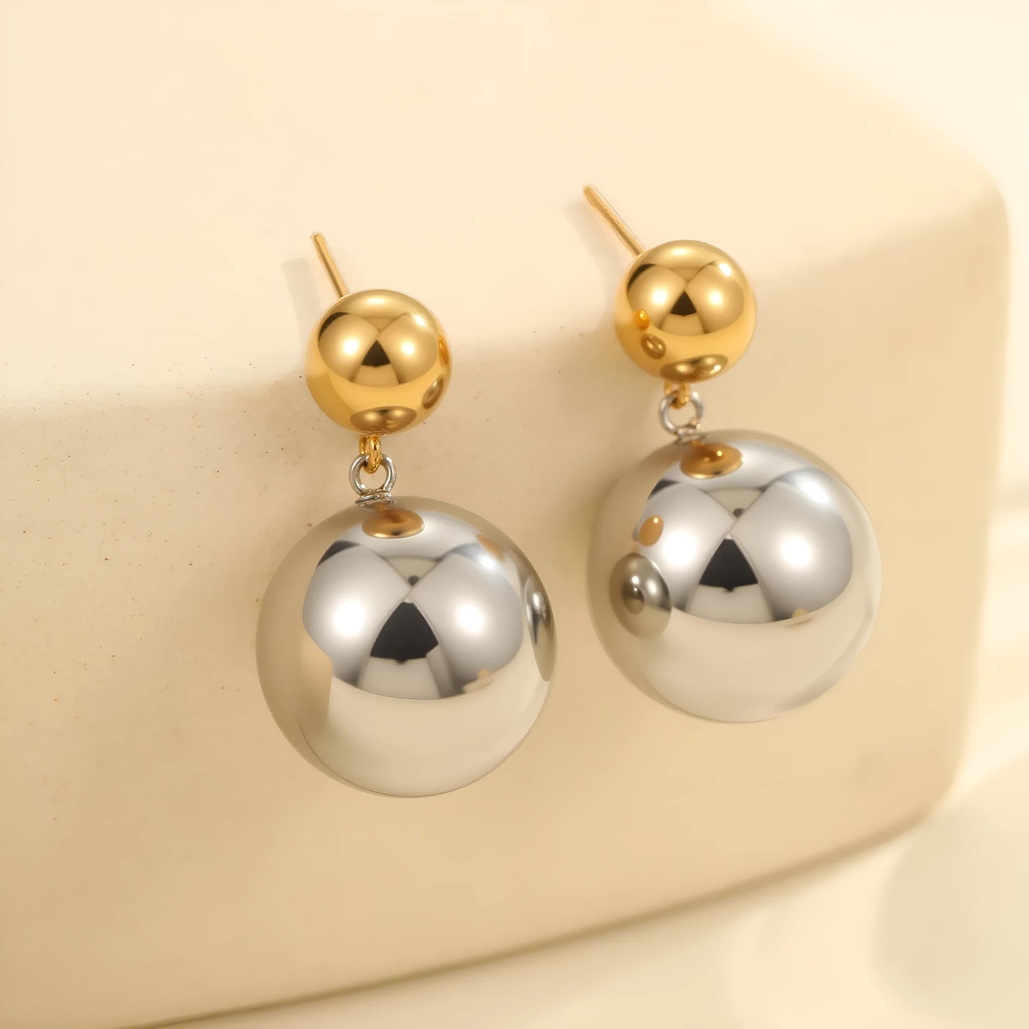 Pair of round bead stud earrings with gold plating and colour-block design on a woman's earlobe.