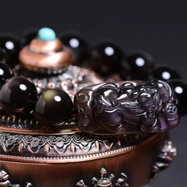 Polished icy obsidian crystal Pi Xiu bracelet with geometric beads on a white background.