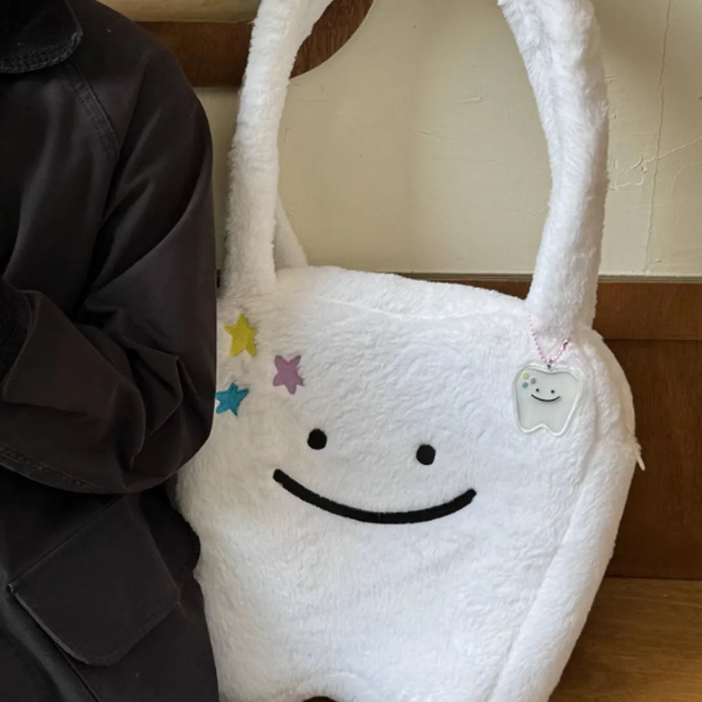 White plush tote bag with tooth decoration and shoulder strap showing zip opening