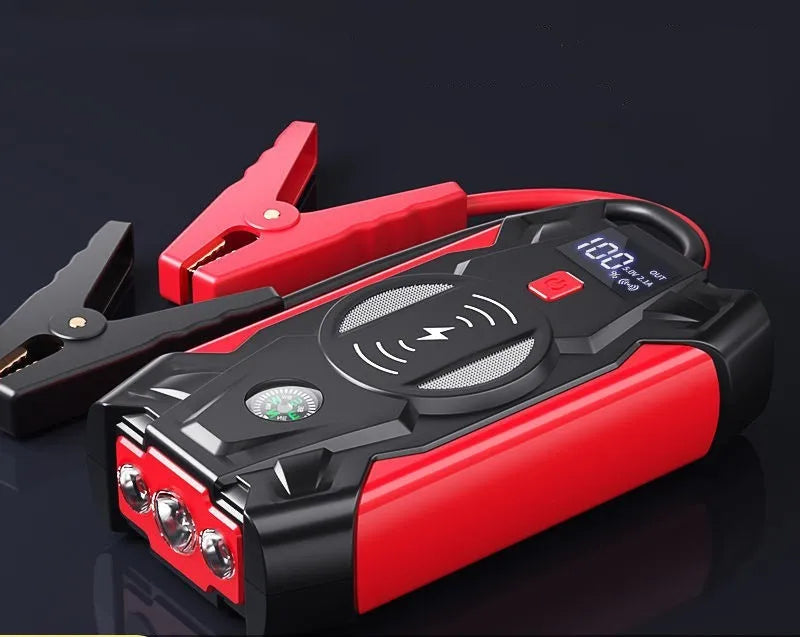 Red portable car jump starter and power bank unit with jumper cables on a table