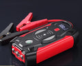 Red portable car jump starter and power bank unit with jumper cables on a table