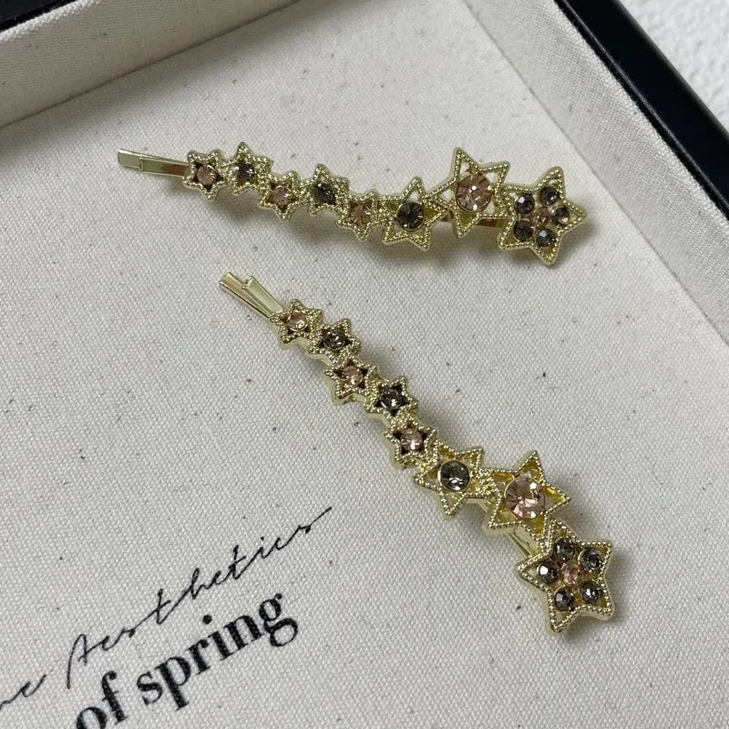 Golden alloy barrette hair clip with rhinestone star decoration and single-word element.