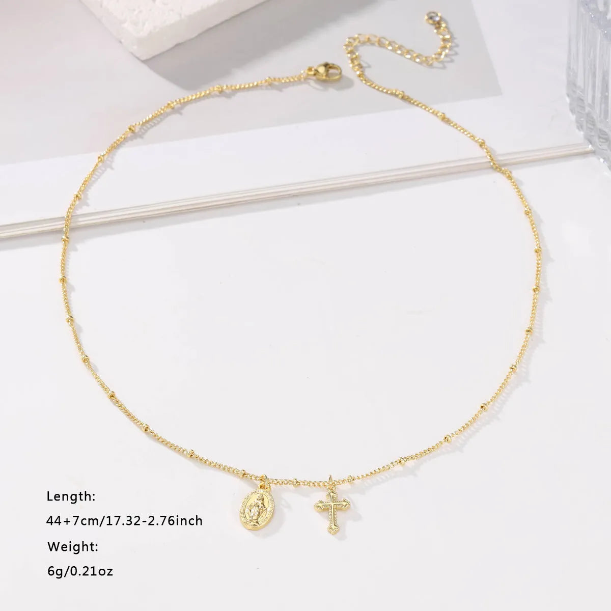 Gold-coloured geometric cross pendant necklace with a Virgin Mary ornament, on a chain.