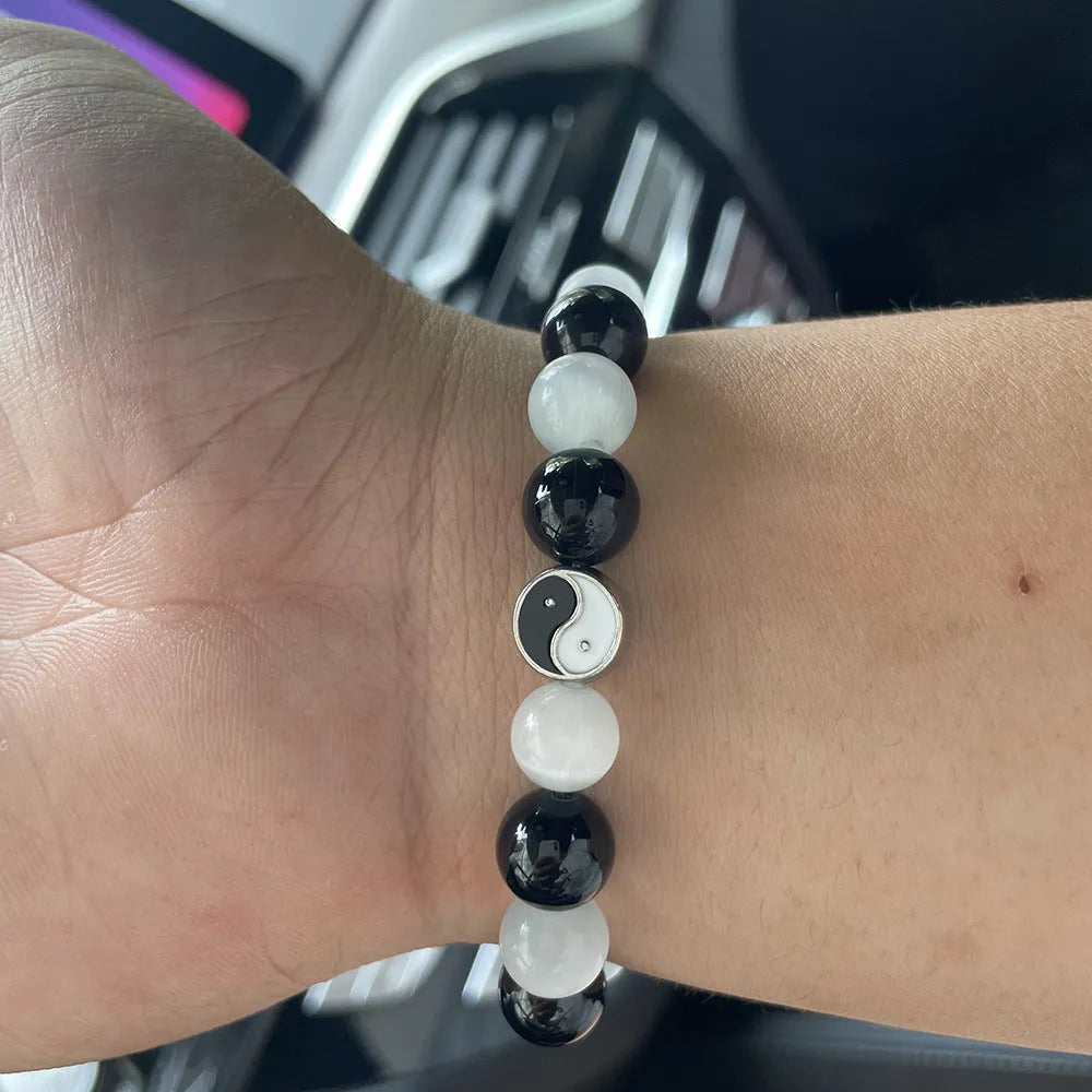 A polished black agate opal beaded bracelet with an ornamental Tai Chi symbol, shown on a wrist.