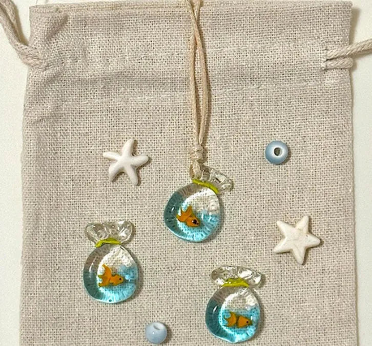 Women's necklace with blue glazed small fish charm pendant on a beige cotton-linen clavicle chain.
