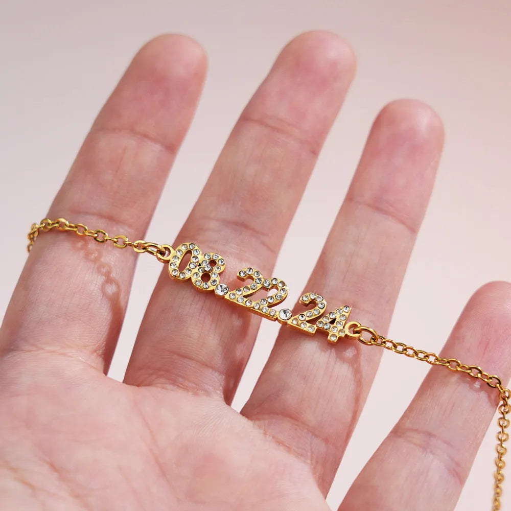 Stainless steel bracelet or necklace with diamond accents around digital numerals in gold, rose gold, or steel colour.