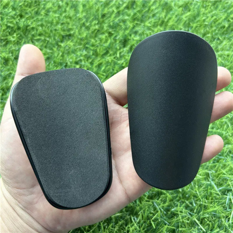 A pair of extra small mini plastic football shin guards, shown in either black or white.