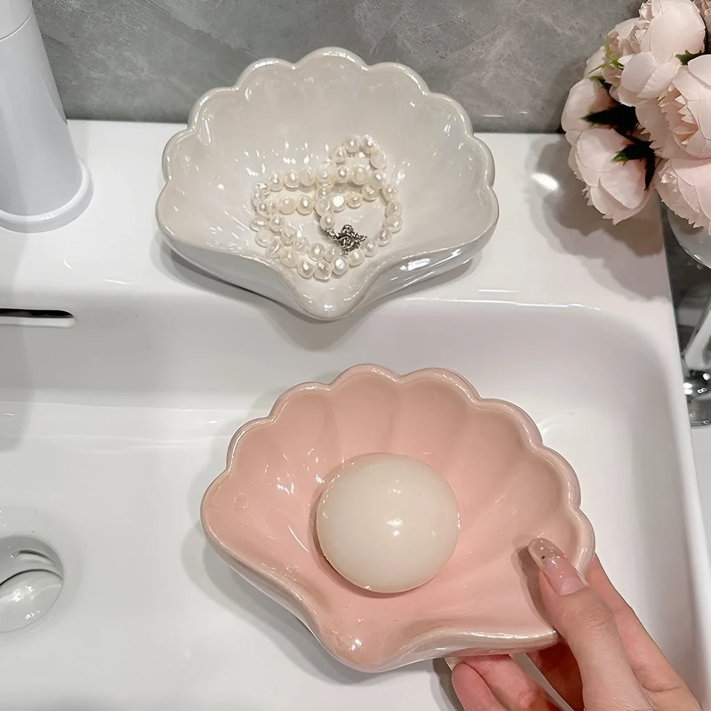 White shell-shaped plastic soap dish for bathroom counter next to pink version.