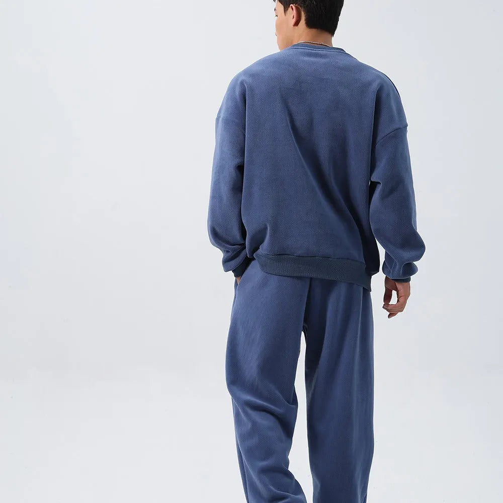 Man wearing a grey polar fleece crew neck coat and matching padded trousers from a casual winter sport suit set.