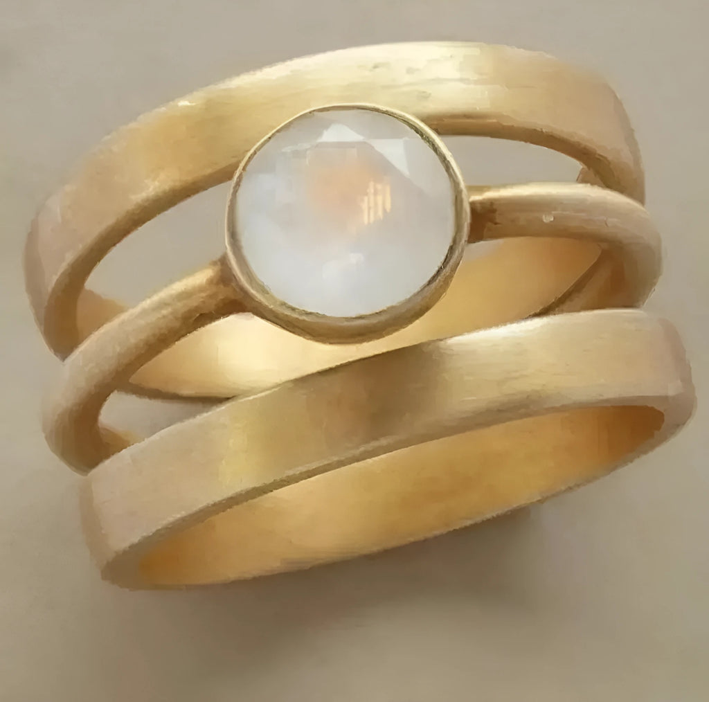 Gold-plated geometric ring with a white chalcedony stone centrepiece on a grey background.