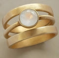 Gold-plated geometric ring with a white chalcedony stone centrepiece on a grey background.