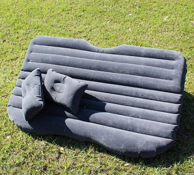 Black inflatable car bed with flocked texture and two pillows, shown inside a car boot.