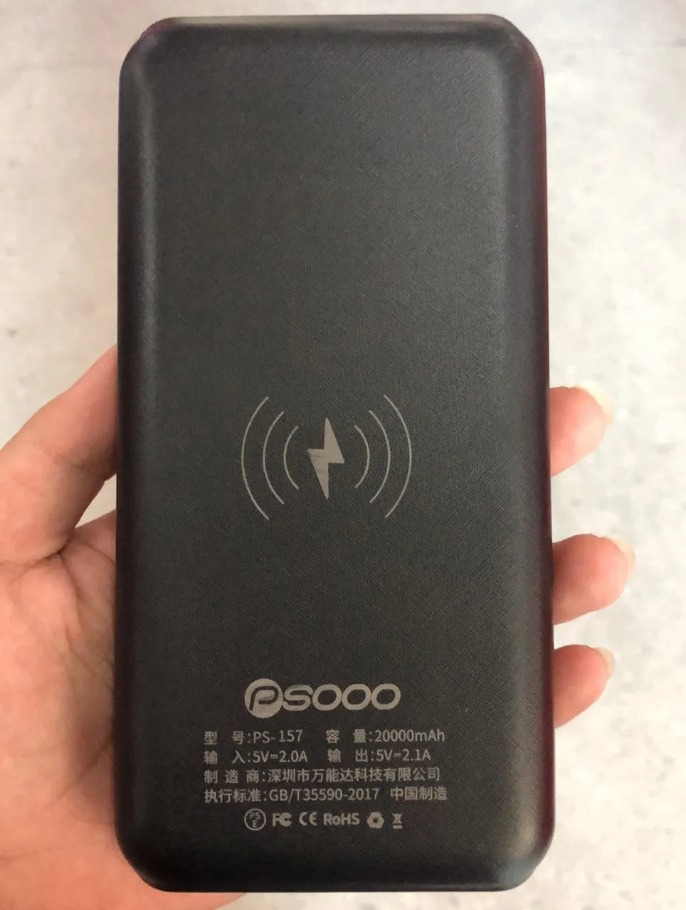 Black portable power bank with Qi wireless charging pad, three USB ports, and an LED flashlight on the front.