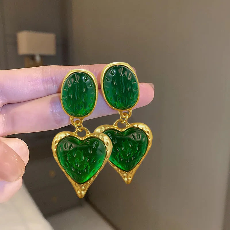 A pair of oval-shaped love heart stud earrings with a pleated surface, shown in one of four colour options.