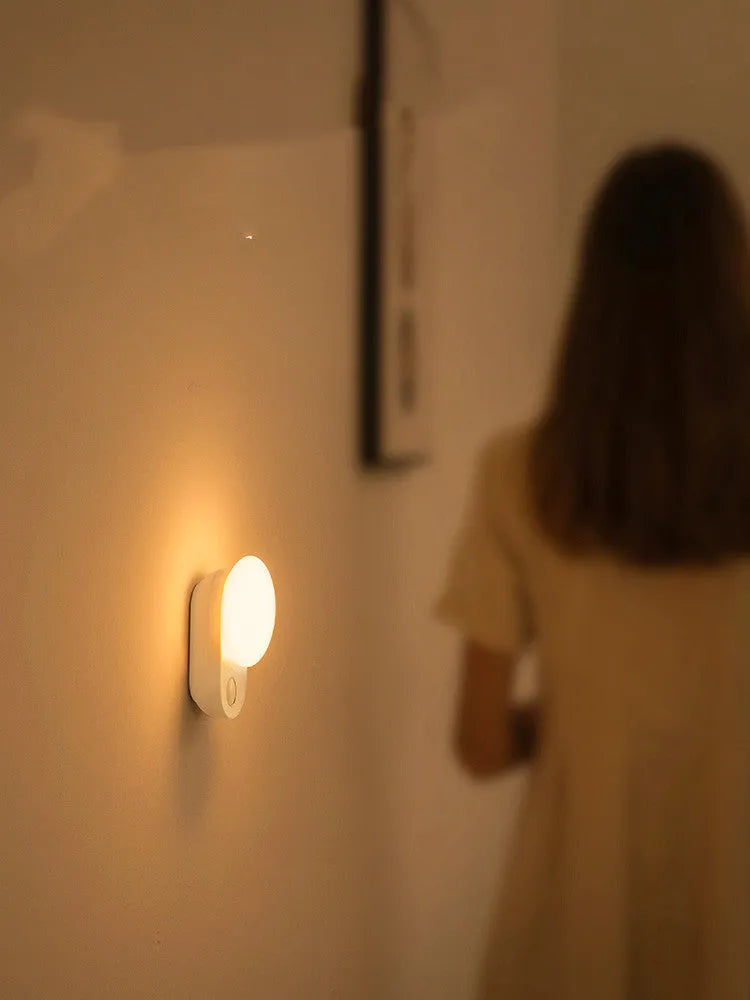White circular rechargeable sensor night light with warm LED illumination for bedside placement
