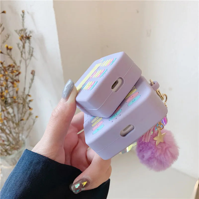 Purple silicone Apple AirPods protective case with attached fur ball pendant on white background