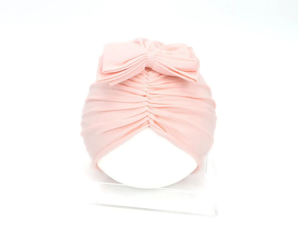 Soft knitted acrylic baby girl turban hat in a solid colour, shown on an infant.