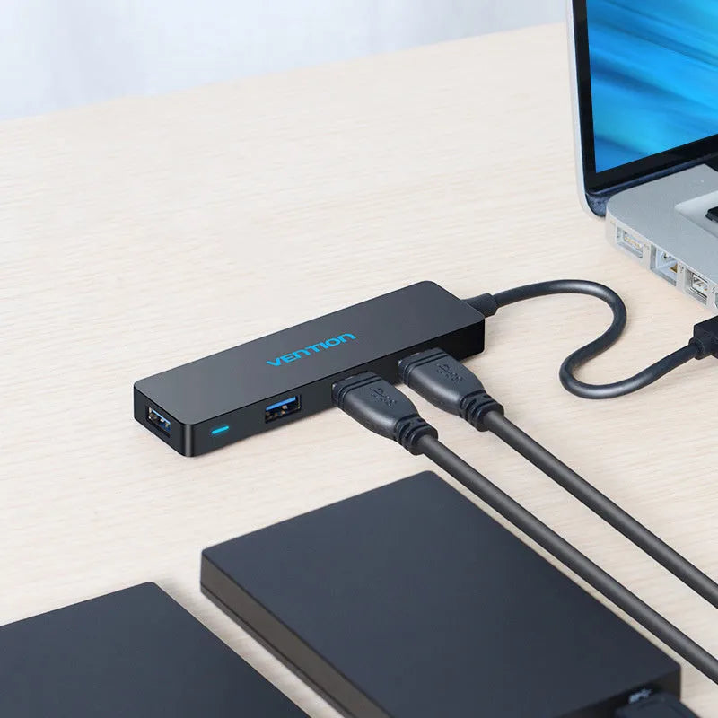 Black four-port USB 3.0 hub with a short cable on a desk next to a laptop