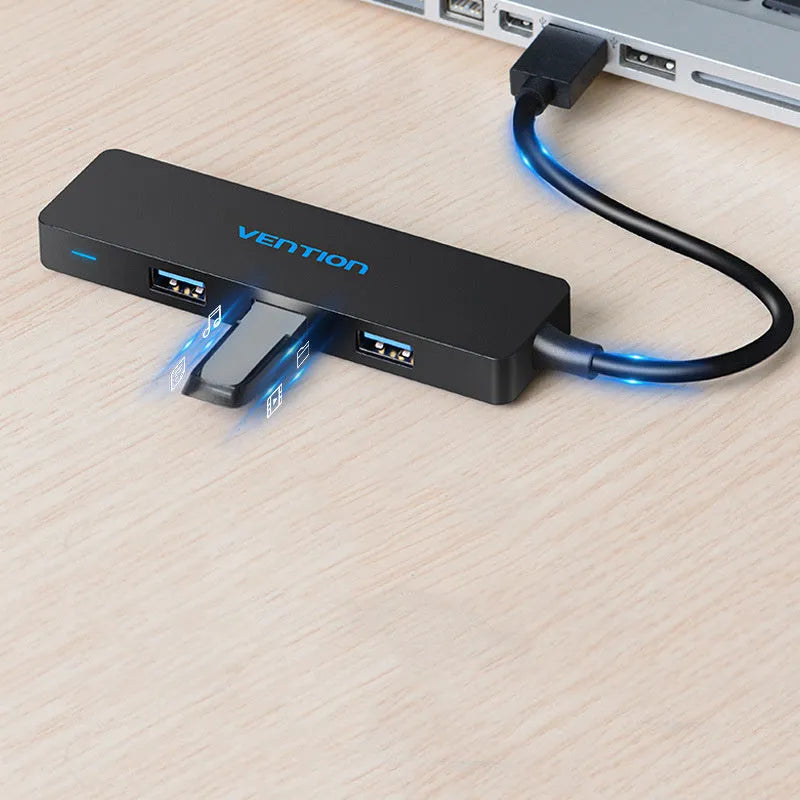 Black four-port USB 3.0 hub with a short cable on a desk next to a laptop