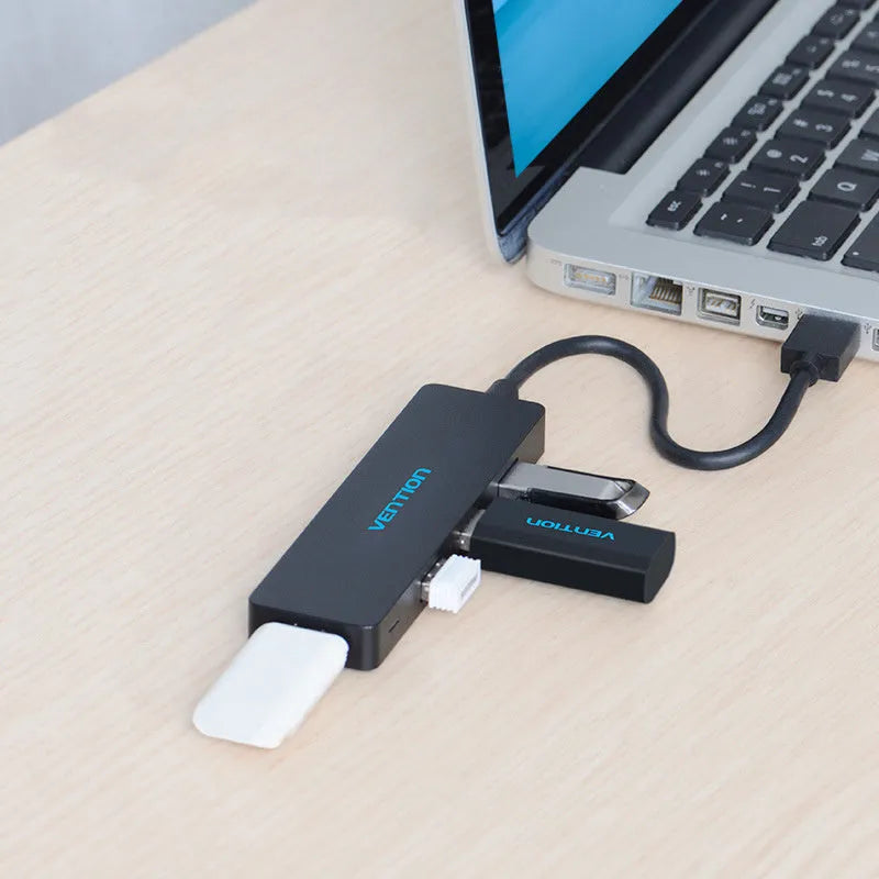 Black four-port USB 3.0 hub with a short cable on a desk next to a laptop