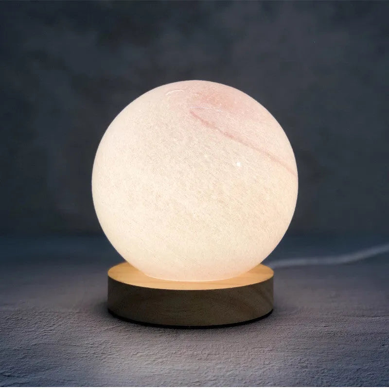 Nordic style USB table lamp with a glass shade shown in one of seven available colours on a bedside table.