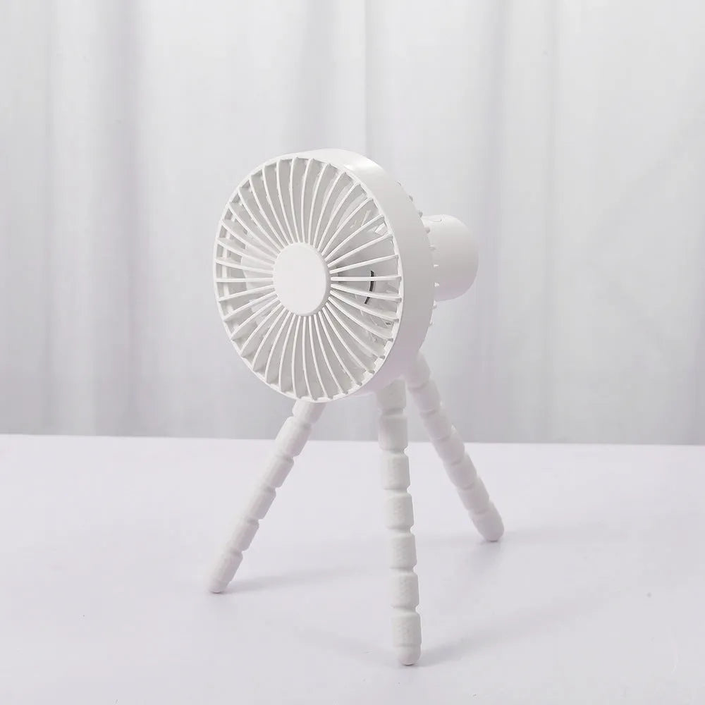 Compact USB desktop fan with flexible black tripod legs and a white fan head on a wooden desk.