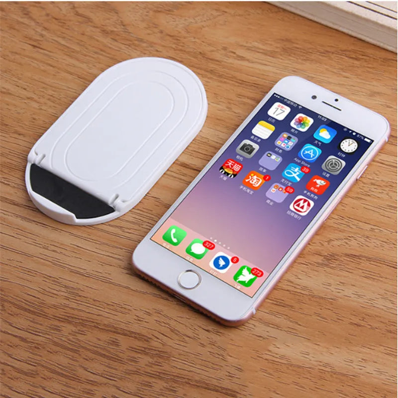 A plastic lazy bracket mobile phone stand on a table, shown in one of six available colours.
