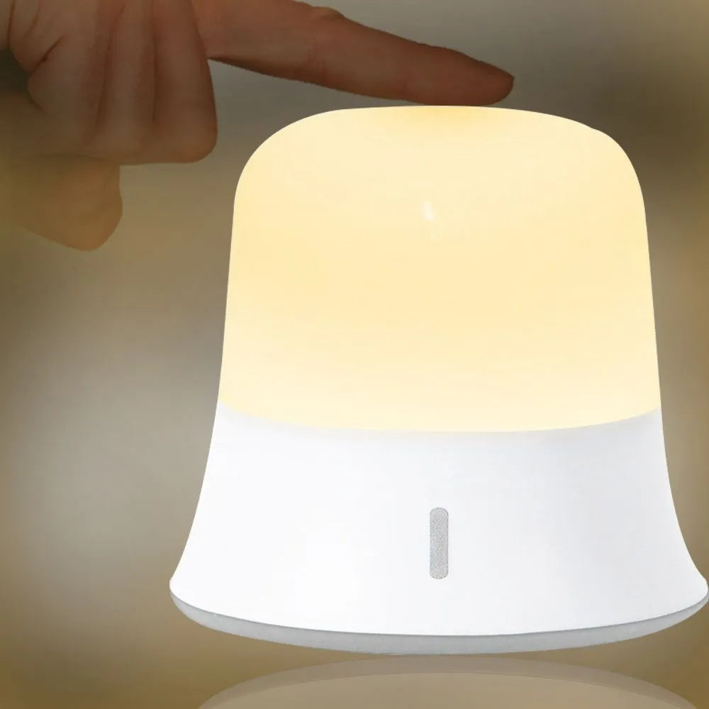 White cylindrical bedside night light with touch controls on a wooden surface.