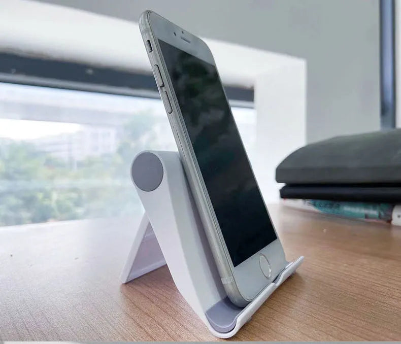 Black PE folding stand holding a mobile phone at an angle on a wooden desk.