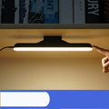 Modern plastic LED desk lamp with touch switch and rechargeable battery on a wooden desk.