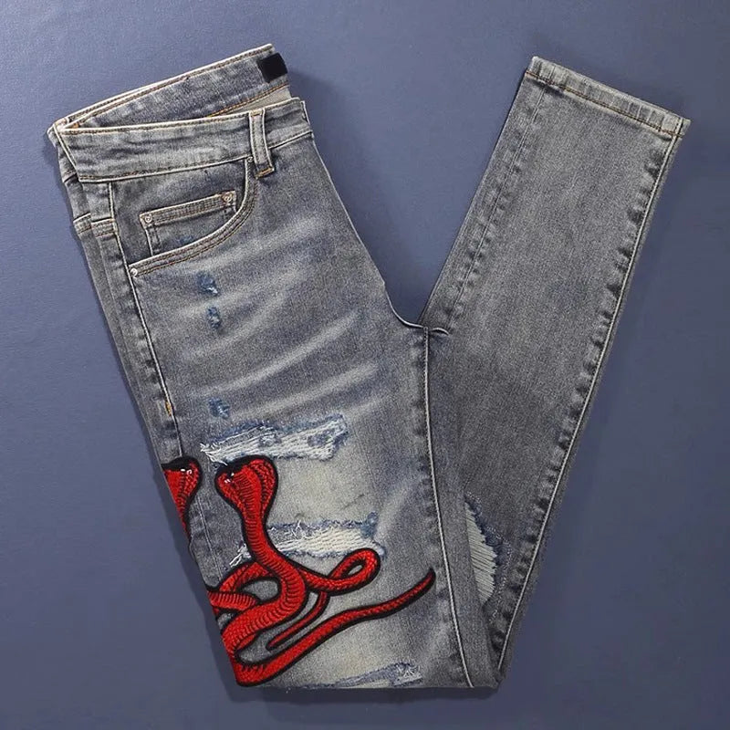 Slim fit light blue jeans with worn patches and embroidery on the legs, showing a washed-out colour.
