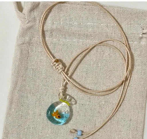 Women's necklace with blue glazed small fish charm pendant on a beige cotton-linen clavicle chain.