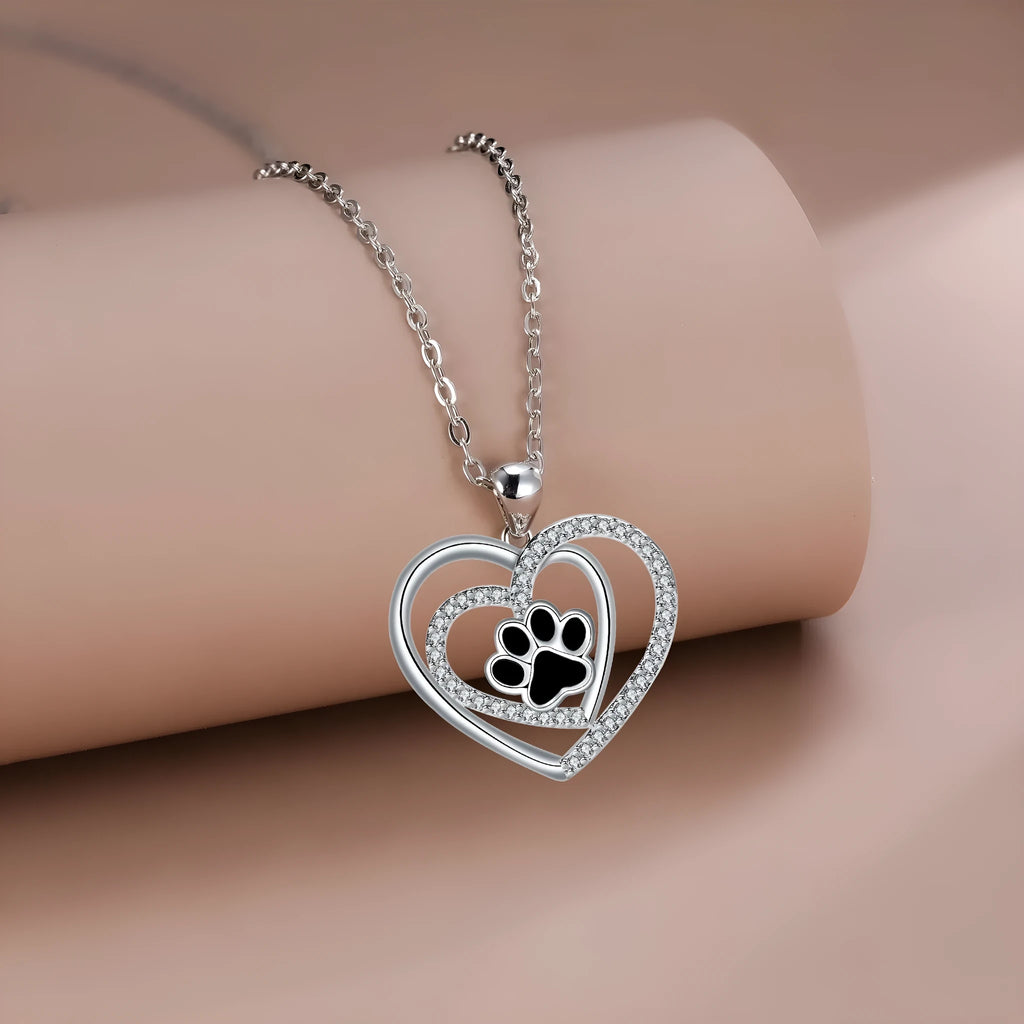 Close-up of a heart-shaped copper necklace pendant featuring a detailed dog's paw print design on a cross chain.