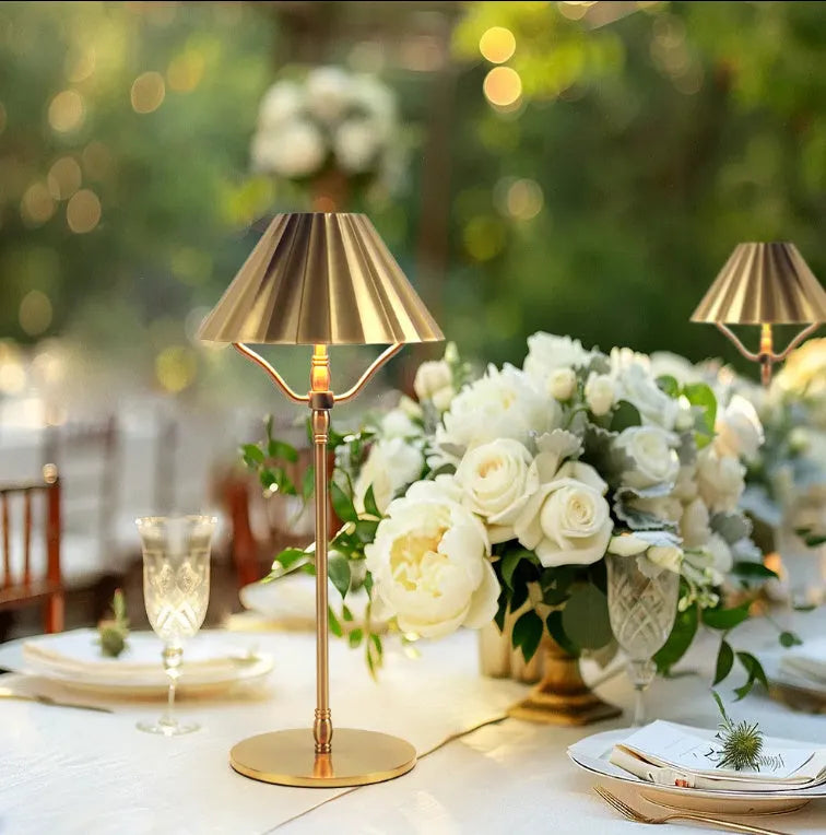 Gold-coloured alloy desk lamp with a fabric shade on a wooden desk.