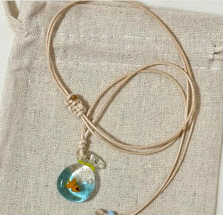 Women's necklace with blue glazed small fish charm pendant on a beige cotton-linen clavicle chain.