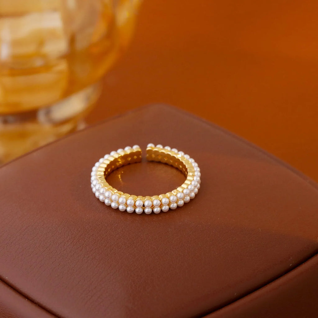 Gold geometric open ring for women with a pearl centre on a white background.
