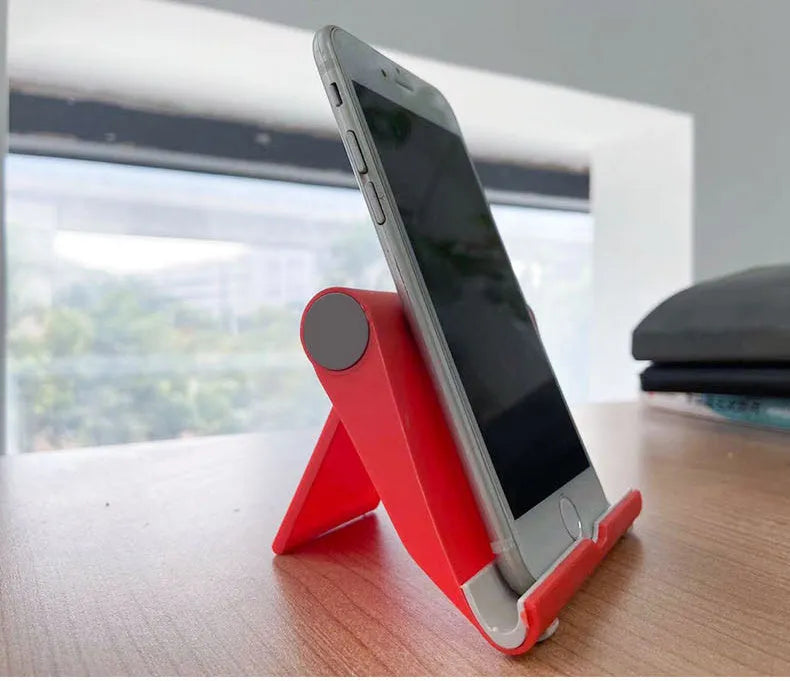 Black PE folding stand holding a mobile phone at an angle on a wooden desk.