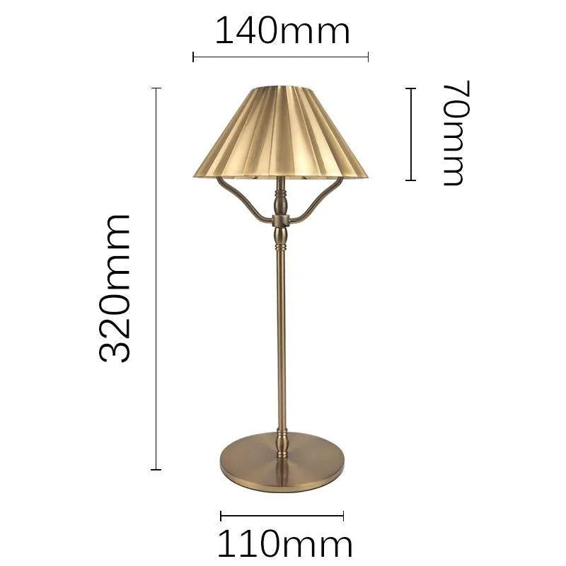 Gold-coloured alloy desk lamp with a fabric shade on a wooden desk.