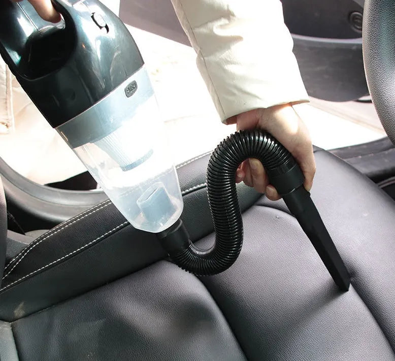 Compact orange handheld vacuum cleaner with nozzle, next to a car's 12V cigarette lighter socket.