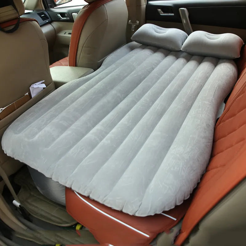 Black inflatable car bed with flocked texture and two pillows, shown inside a car boot.