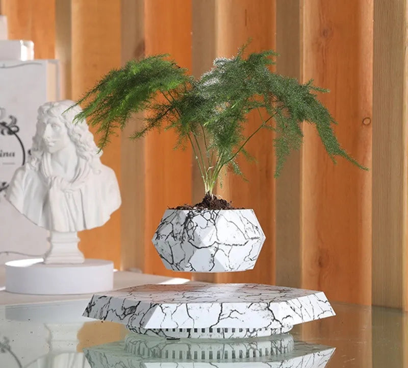 Marble-coloured levitating plant pot floating above magnetic base with small indoor plant