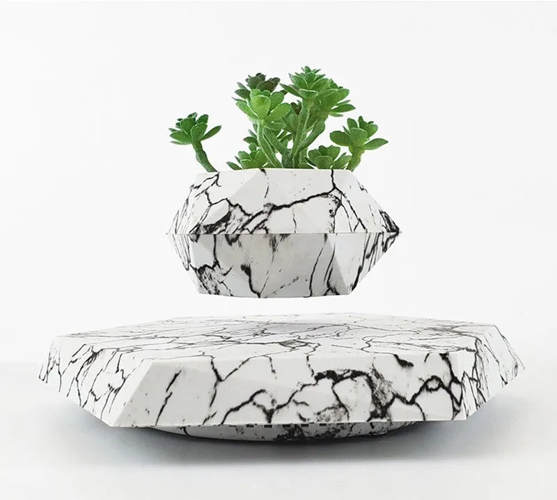 Marble-coloured levitating plant pot floating above magnetic base with small indoor plant