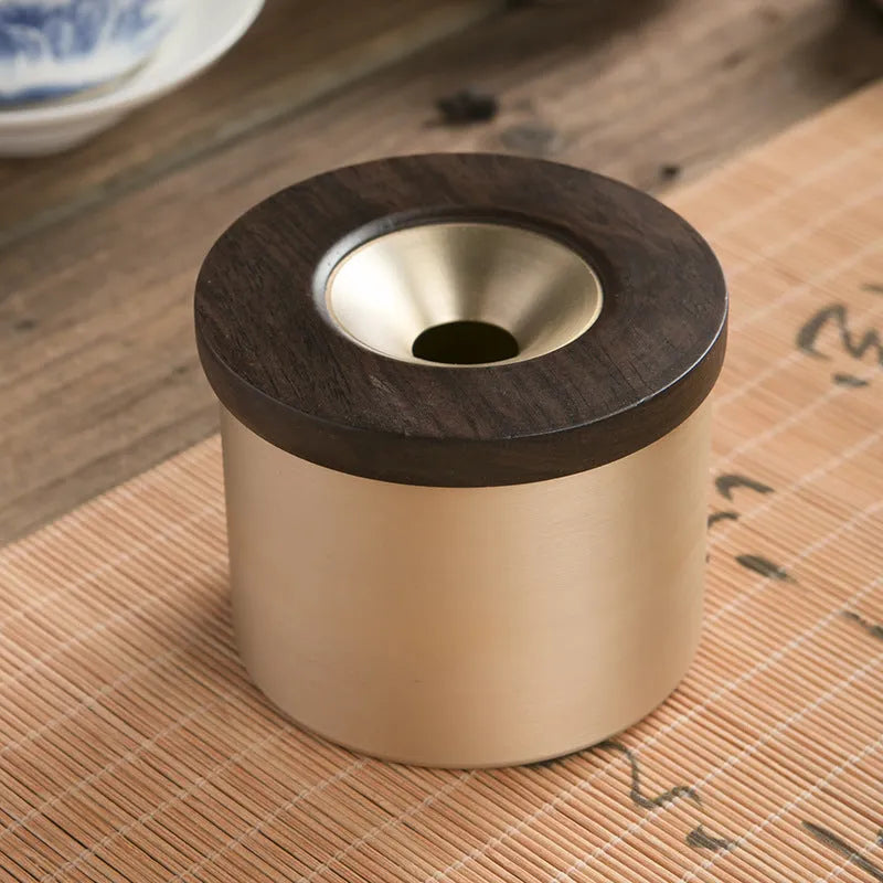 Brass-coloured copper ashtray with a wooden lid featuring a central hole, on a tabletop.