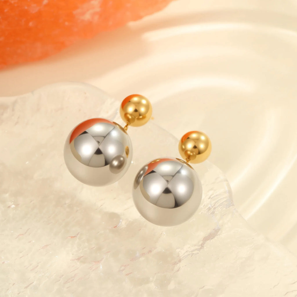 Pair of round bead stud earrings with gold plating and colour-block design on a woman's earlobe.