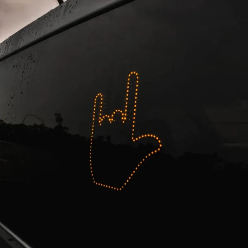 Black plastic LED car gesture light showing illuminated middle finger sign on dashboard
